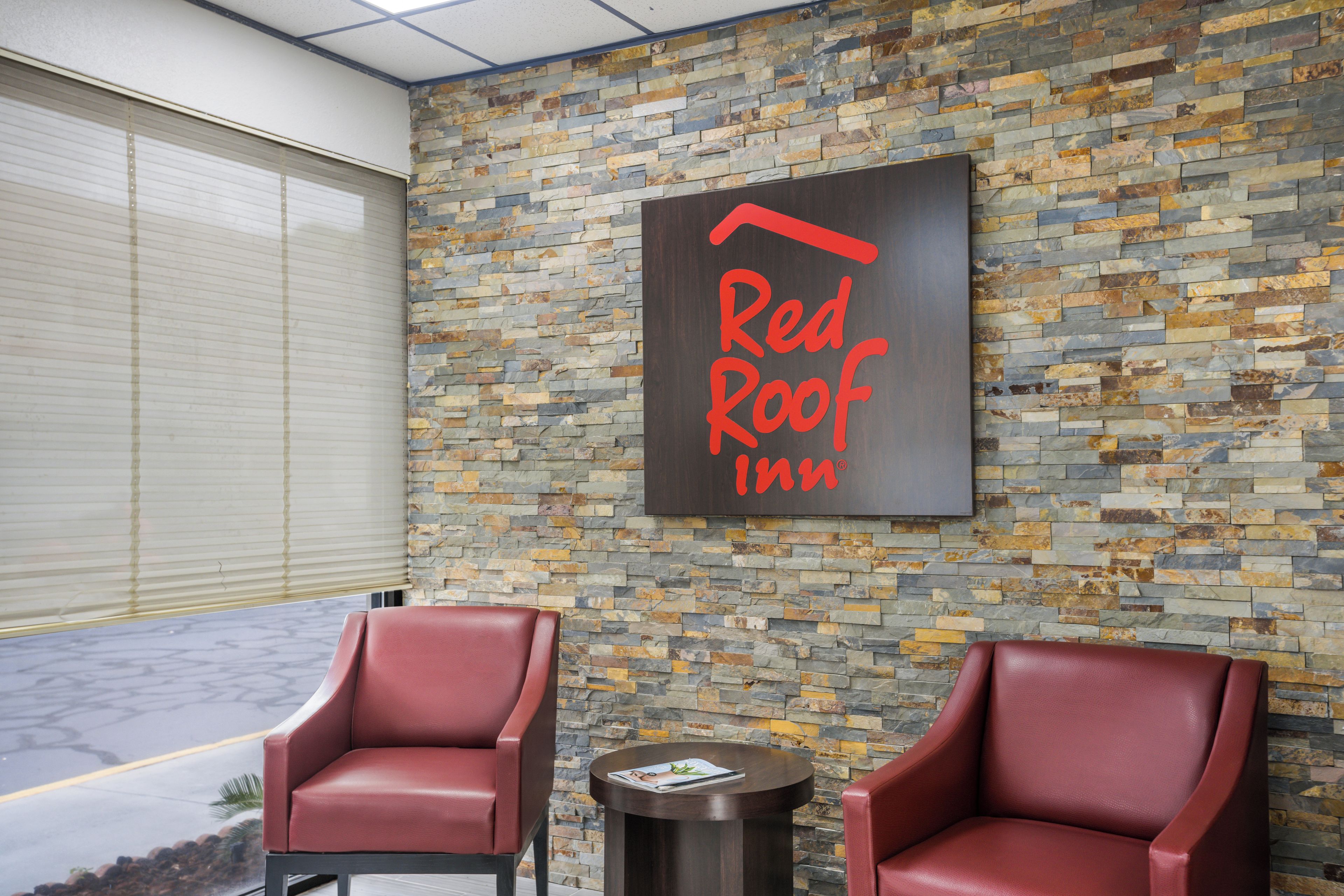 Punainen Red Roof Inn -kyltti karkeapintaisessa kiviseinässä, kaksi nahkaista nojatuolia ja pieni pyöreä pöytä, jonka päällä on lehti.