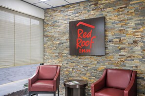 A Red Roof Inn sign on a textured stone wall, two leather chairs, and a small round table with a magazine. - Red Roof Inn Savannah - Southside/Midtown (Savannah)