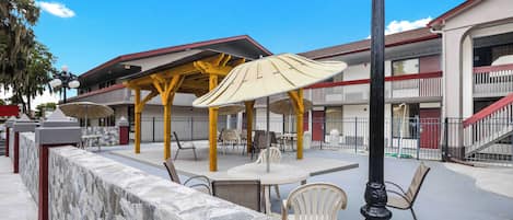 Un patio al aire libre con muros de piedra, mobiliario exterior y una zona de estar cubierta con sombrillas.