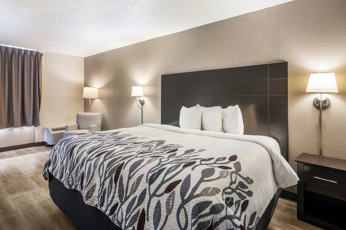 A hotel room with a large bed, two bedside lamps, a chair, and a nightstand.