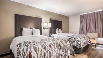 Quarto de hotel com duas camas, uma mesa de cabeceira, uma cadeira e uma janela com cortinas.