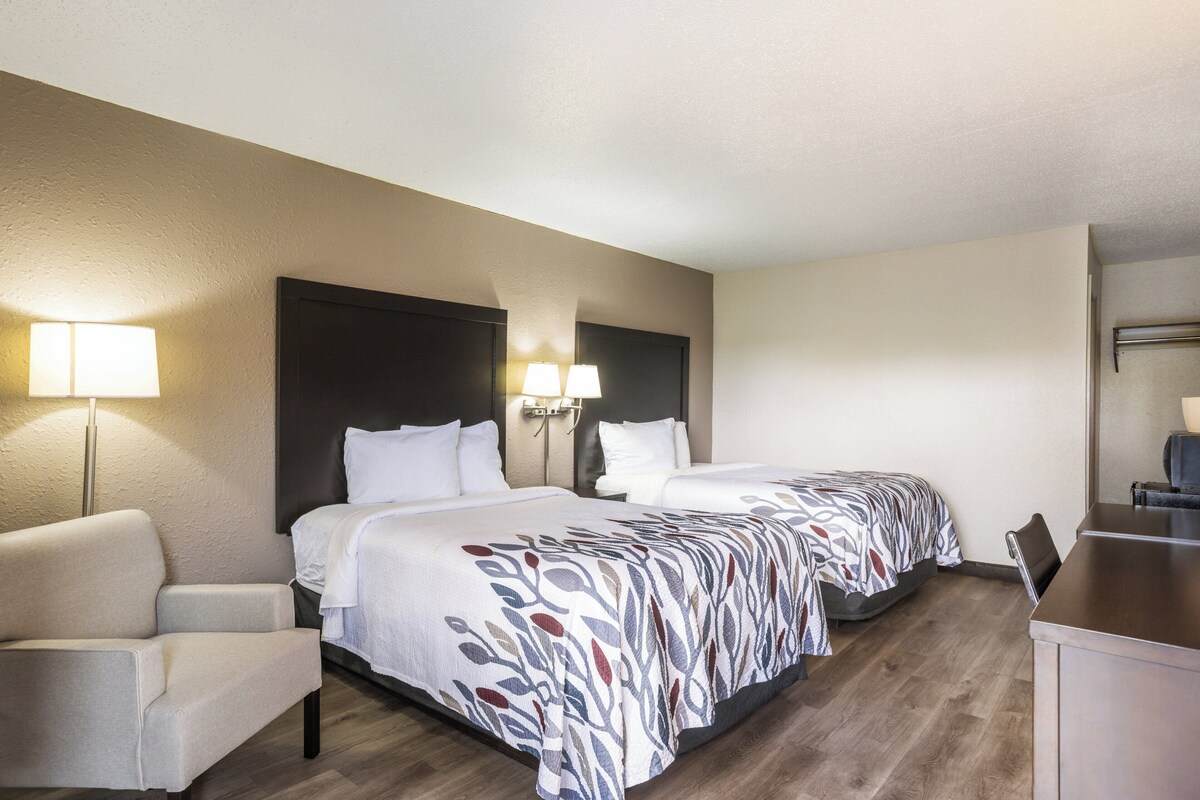 A hotel room with two beds, a desk, and a chair.