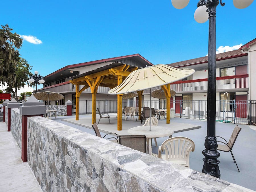 An outdoor patio area with tables and chairs, a stone wall, and a building with balconies in the background.
