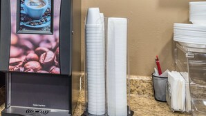 Een koffieapparaat met een digitaal scherm, een stapel papieren bekertjes en een muur met een afbeelding van palmbomen.