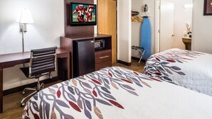 Ein Hotelzimmer mit zwei Betten, einem Schreibtisch, einem Sessel, einem Fernseher, einer Mikrowelle und einem Kleiderschrank.