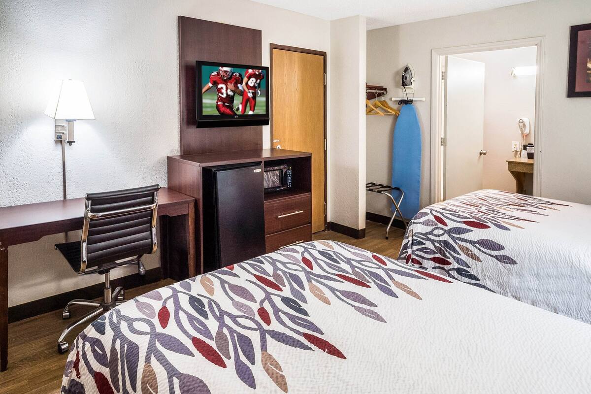 Ein Hotelzimmer mit zwei Betten, einem Schreibtisch, einem Sessel, einem Fernseher, einer Mikrowelle und einem Kleiderschrank.