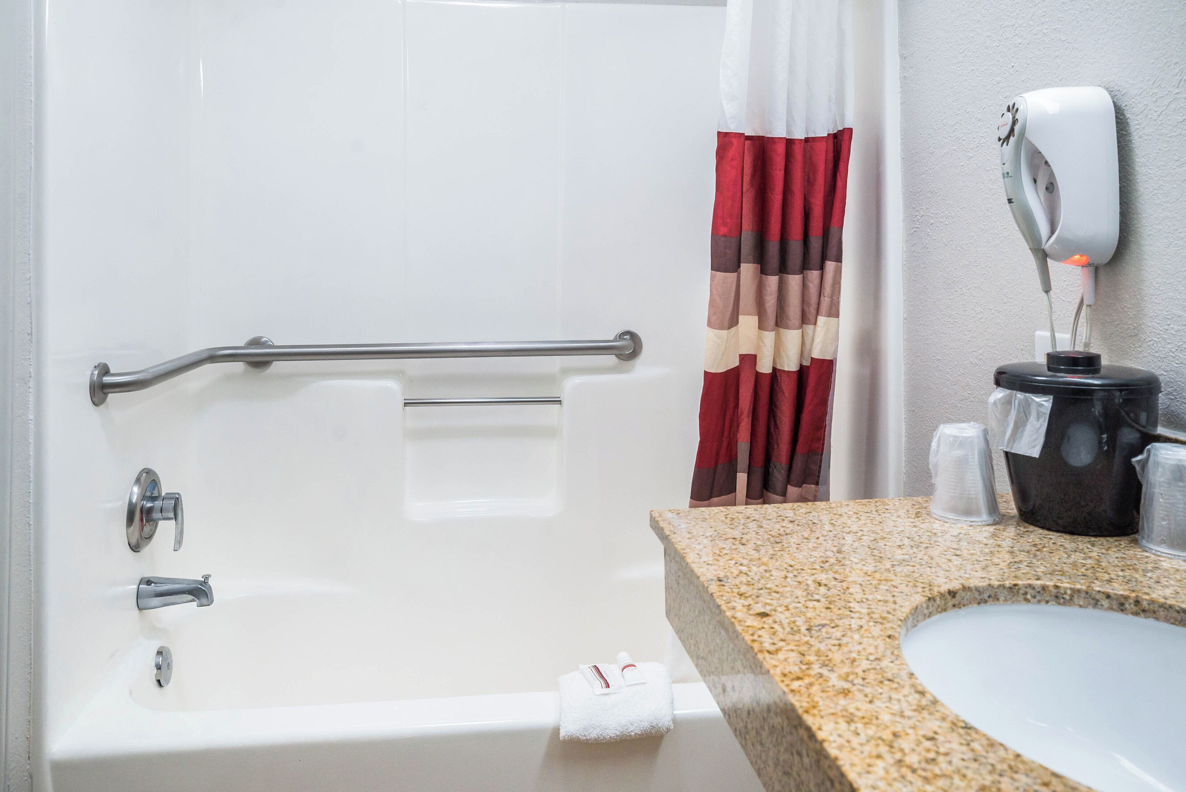 Ein Badezimmer mit einer Badewanne, einer Haltestange, einem Handtuchhalter, einer Duschvorhang und einem Seifenspender sowie einer Arbeitsplatte aus Granit.