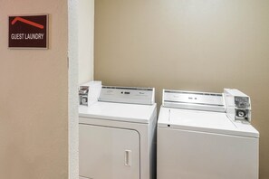 Un espace buanderie à la disposition des clients, équipé de deux machines à laver et d’un panneau indiquant son emplacement.