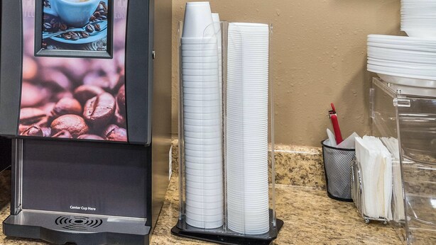 Eine Kaffeemaschine mit digitalem Display, gestapelten Papierbechern und einem Kaffeeausgabesystem auf einer Theke.