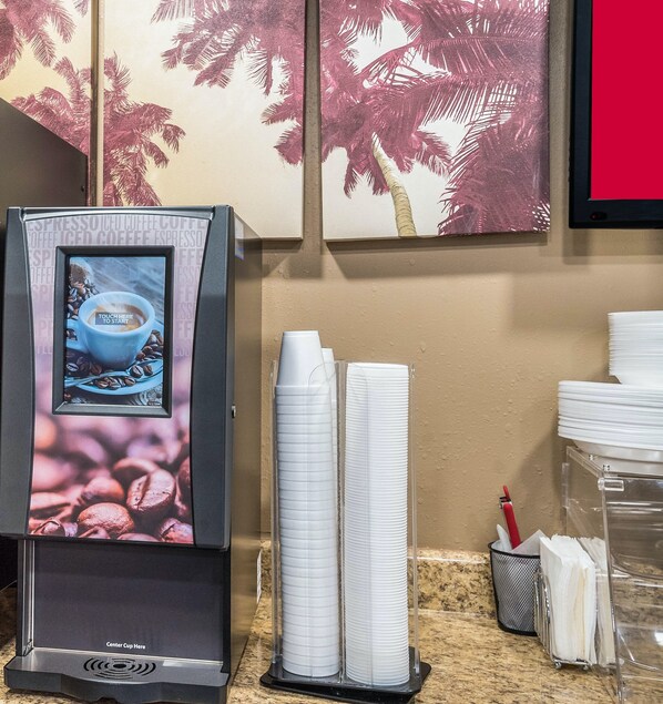 Una máquina de café con pantalla digital, vasos de papel apilados y dispensador de café sobre una encimera.