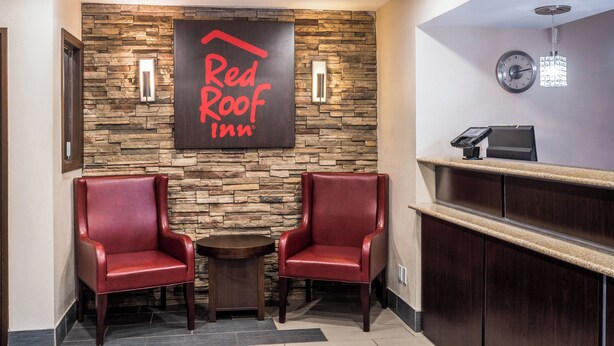 Un espace d’accueil de l’hôtel Red Roof Inn, avec un mur en pierre, deux fauteuils en cuir, une petite table et un comptoir de réception.