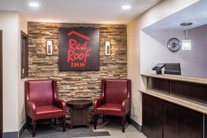Un espace d’accueil de l’hôtel Red Roof Inn, avec un mur en pierre, deux fauteuils en cuir, une petite table et un comptoir de réception.