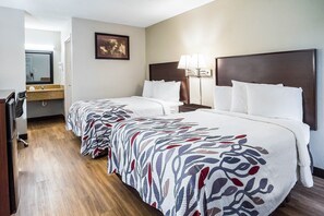 Habitación de hotel con dos camas, un escritorio, una silla, un espejo y una mesita de noche con lámparas.