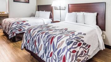 Twin beds with patterned bedspreads, a bedside table, a lamp, and a wall-mounted light fixture in a hotel room.