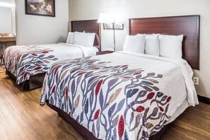 Deux lits jumeaux avec des couvre-lits à motifs, une table de chevet, une lampe et un luminaire fixé au mur dans une chambre d’hôtel.