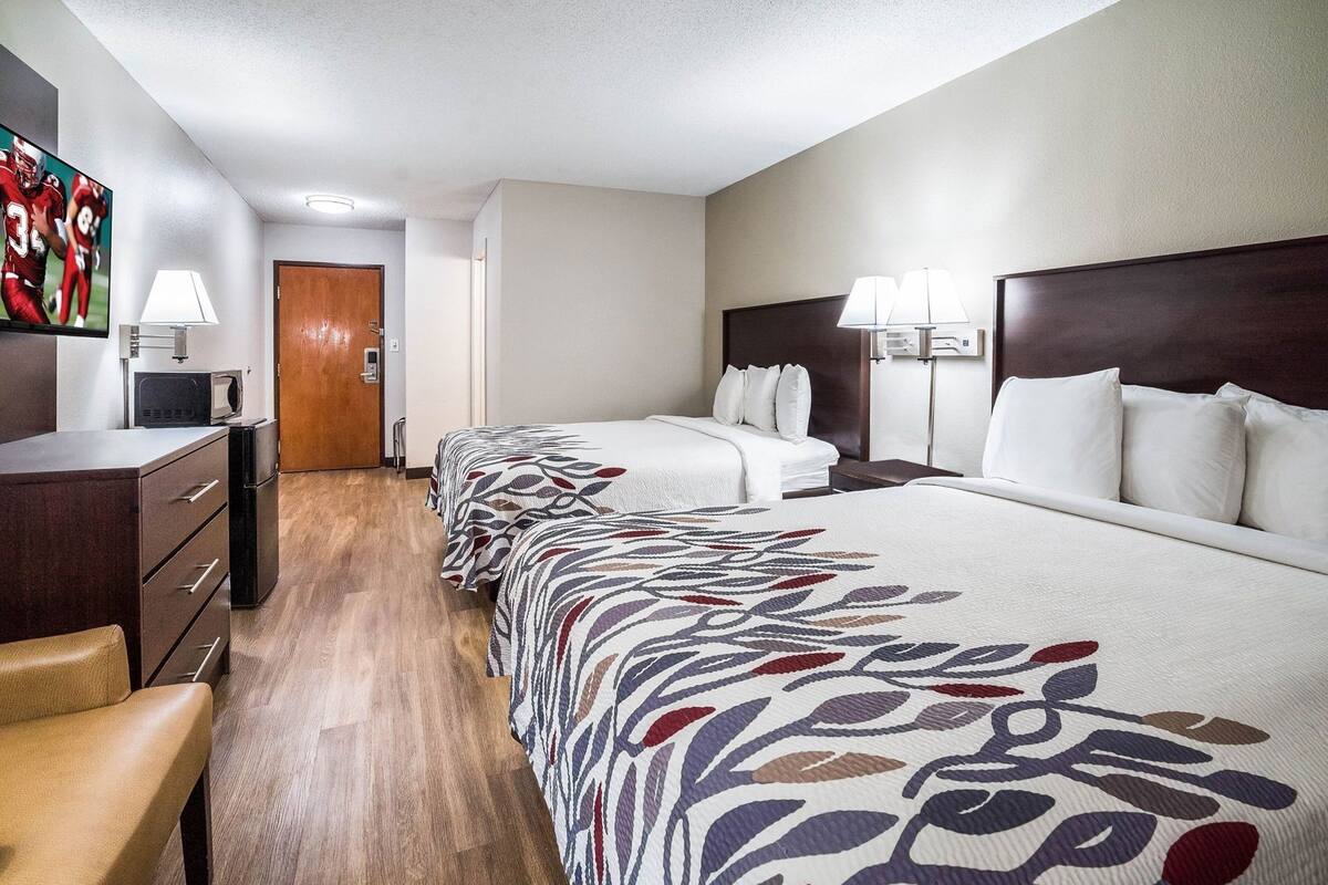 Ein Hotelzimmer mit Schreibtisch, zwei Betten, einem Sessel und einer Tür.