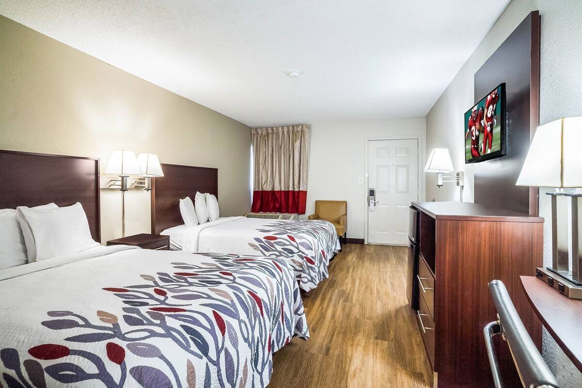 Ein Hotelzimmer mit zwei Betten, einem Schreibtisch, einem Fernseher und einer Tür.