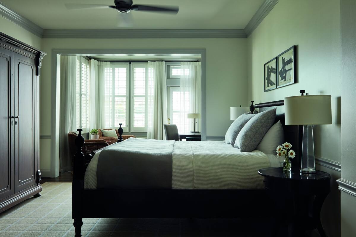 A bedroom with a large bed, a nightstand, a lamp, a dresser, and a window with curtains.