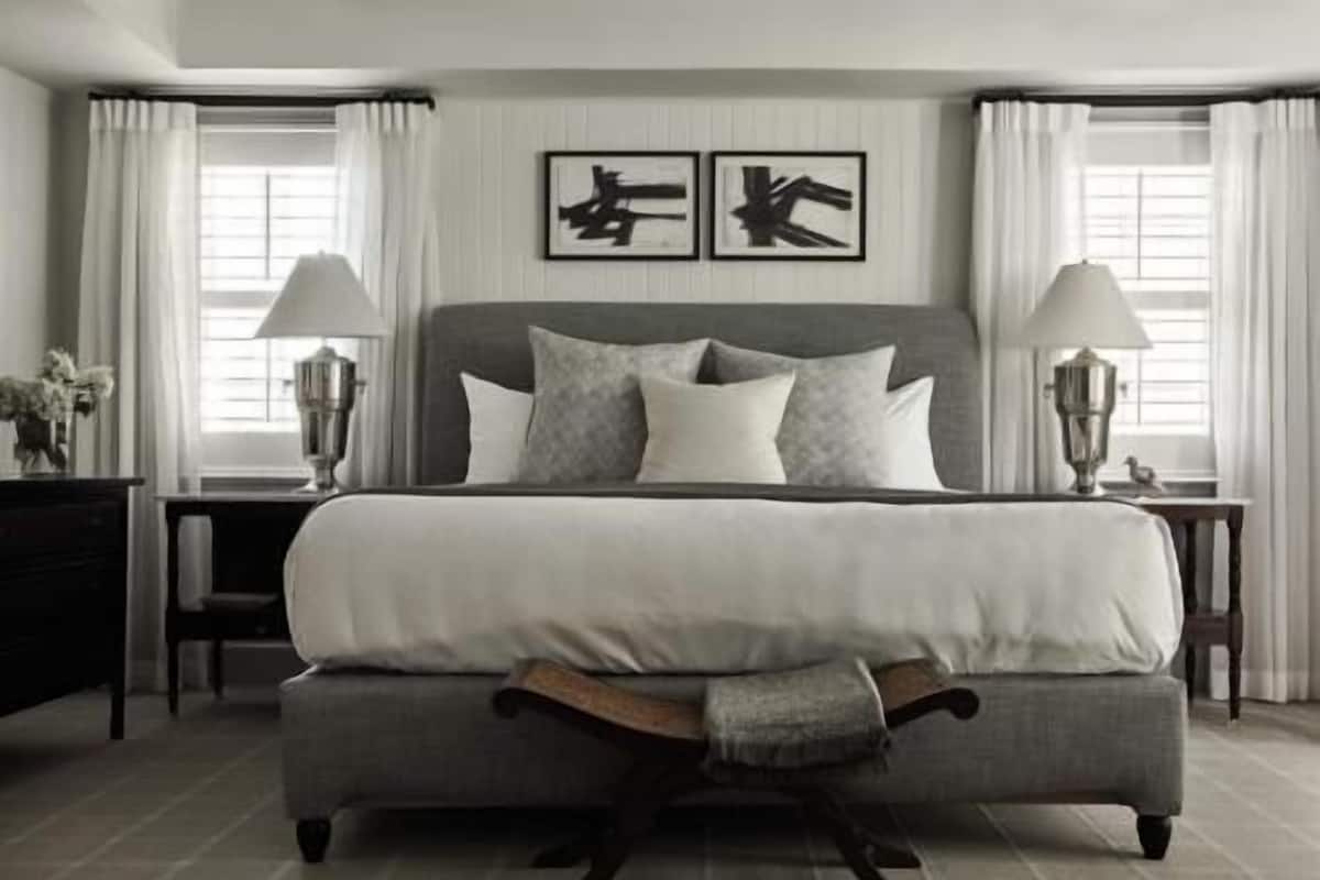 A bedroom with a large bed, two bedside tables with lamps, a nightstand, and a chair.