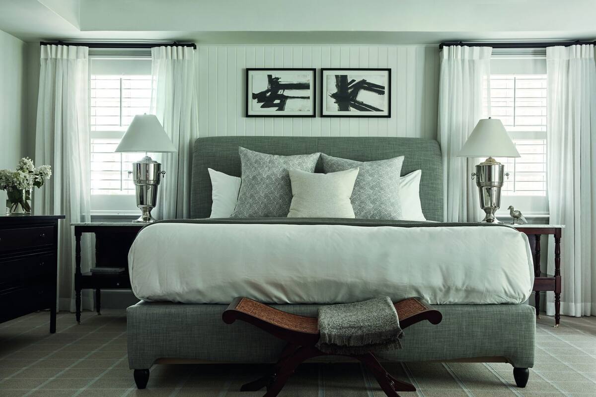 A bedroom with a large bed, two bedside tables with lamps, a dresser, and a wall-mounted artwork.