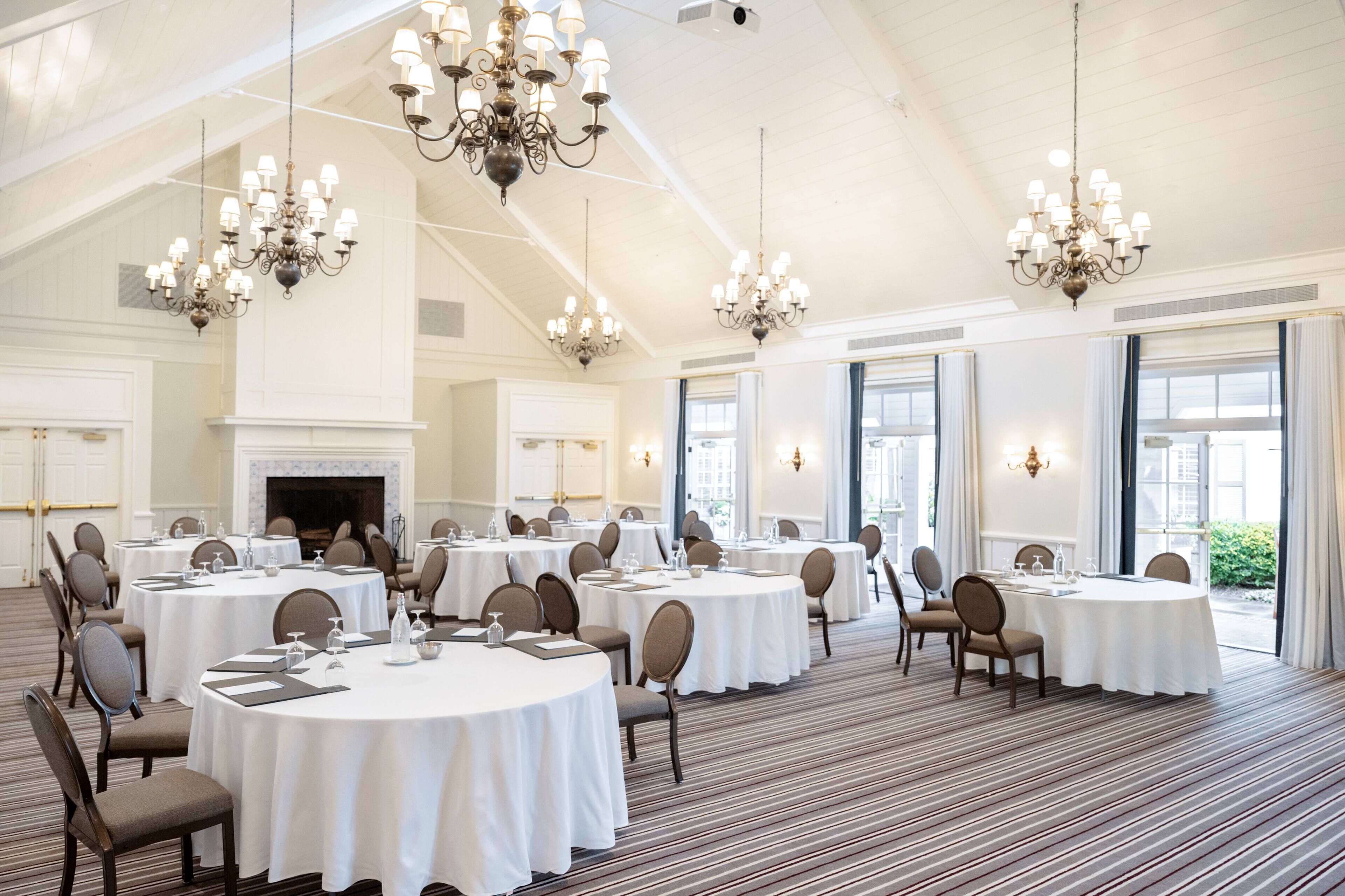 Un amplio y bien iluminado salón de banquetes con mesas redondas, sillas y candelabros.