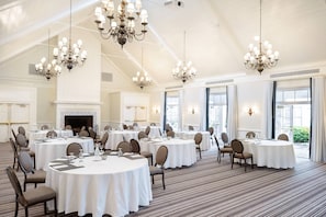 Un amplio y bien iluminado salón de banquetes con mesas redondas, sillas y candelabros.