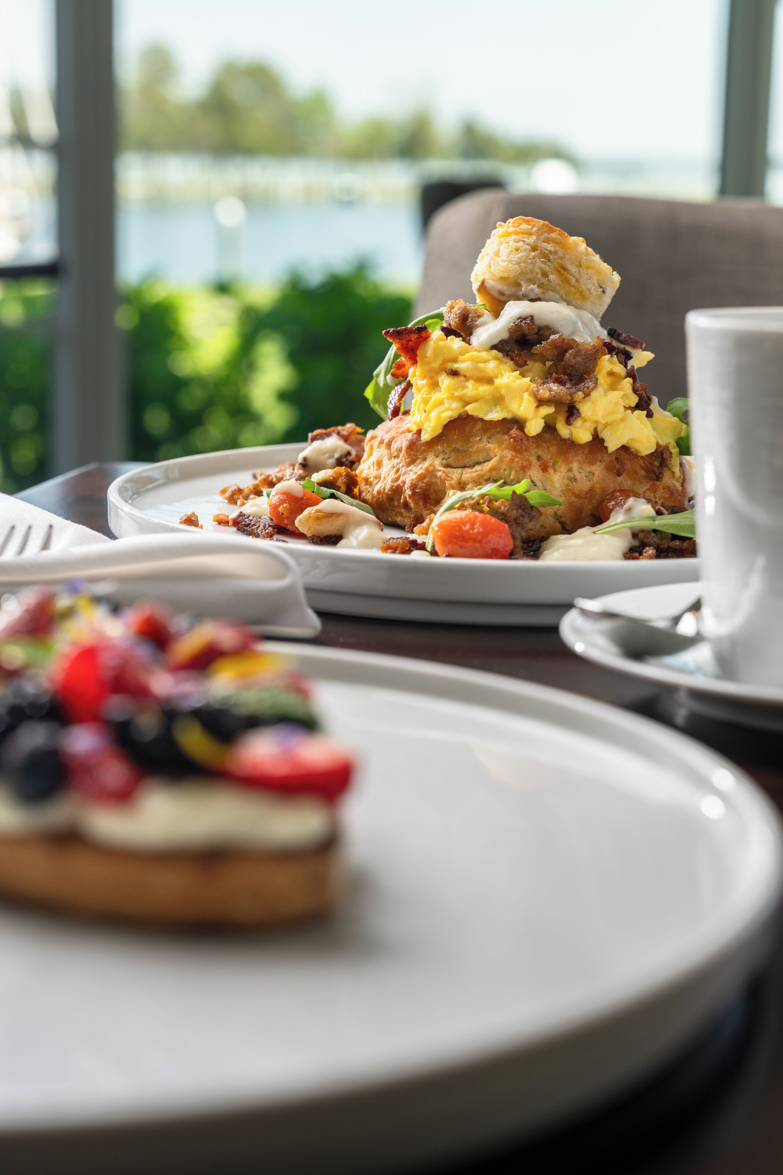 A breakfast setting with a plate of scrambled eggs, bacon, and toast, a cup of coffee, and a dessert on a tray.