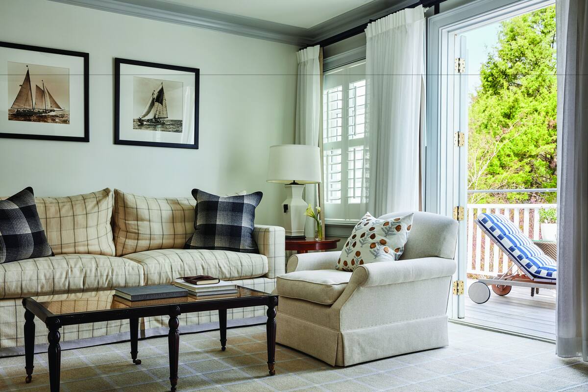 A living room with a sofa, armchair, coffee table, and a balcony with a sun lounger.