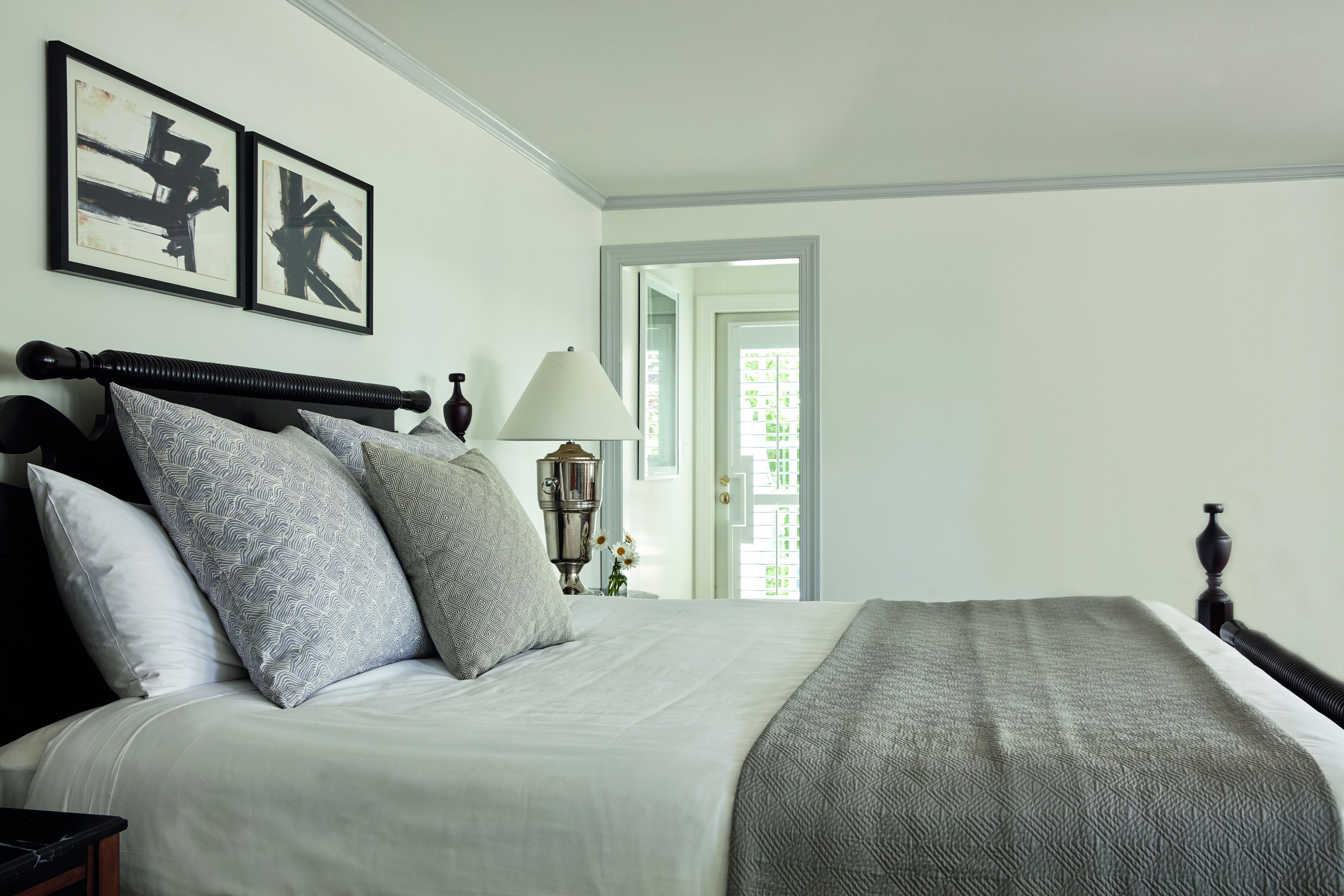 A neatly made bed with a patterned blanket, a bedside table with a lamp, and two framed artworks on the wall.