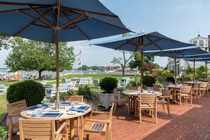 An outdoor patio with tables and chairs, umbrellas, and a view of the water.