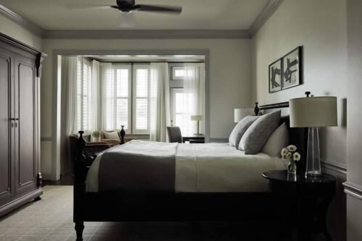 A hotel room with a bed, bedside table, lamp, and a view of the outside through large windows.