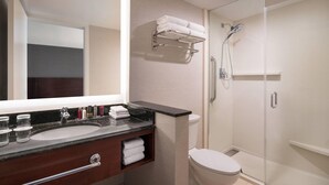 A modern bathroom with a large mirror, a sink with a marble countertop, a toilet, and a glass-enclosed shower area.