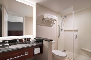 Une salle de bain moderne avec un grand miroir, un lavabo doté d’un plan de toilette en marbre, des toilettes et une douche séparée par une paroi de verre.