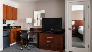 A hotel room with a kitchenette, a TV, a desk with a chair, and a bed.