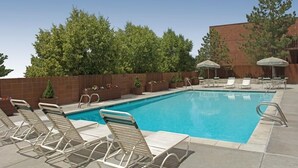 A swimming pool with lounge chairs and umbrellas, surrounded by a brick wall and trees.