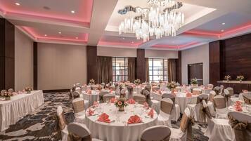 Un salón de banquetes con mesas redondas, manteles blancos y sillas adornadas con cintas doradas.