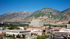 A downtown area with a prominent Zions Bank building, surrounded by mountains and various commercial buildings.