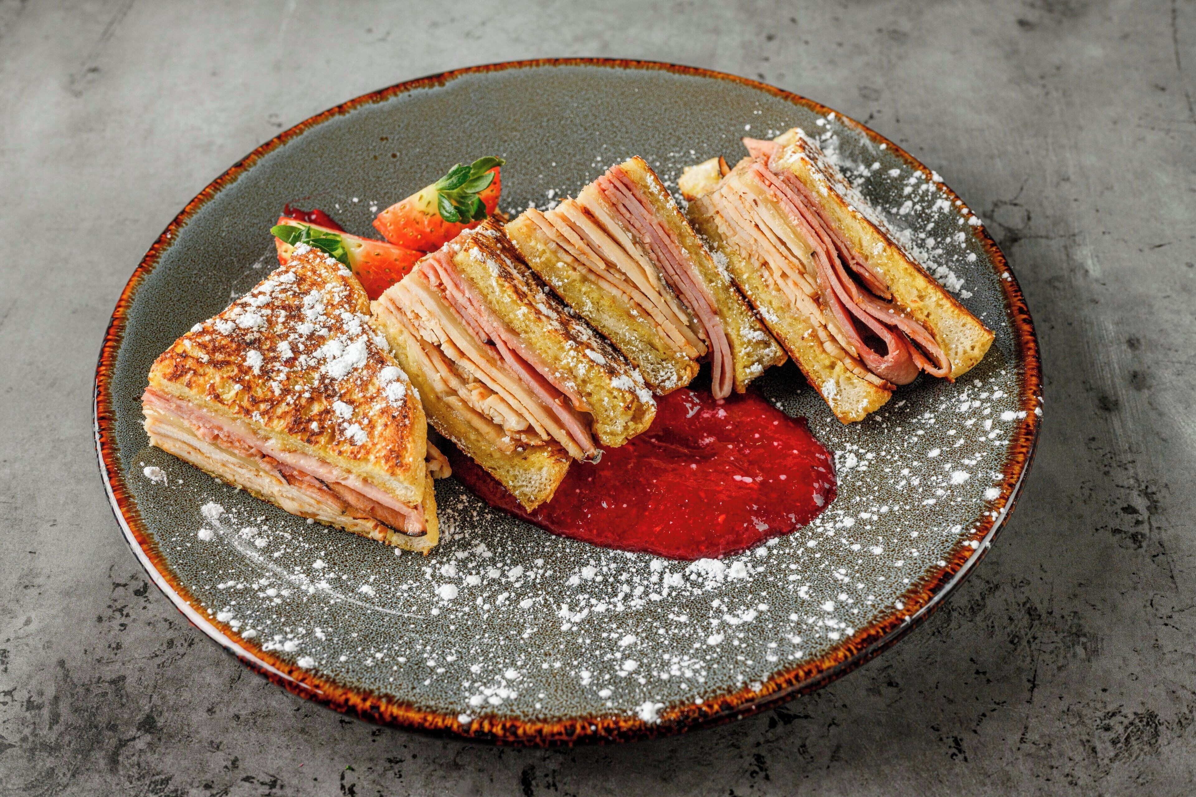 A plate with a layered sandwich, a strawberry, and a dollop of red sauce.