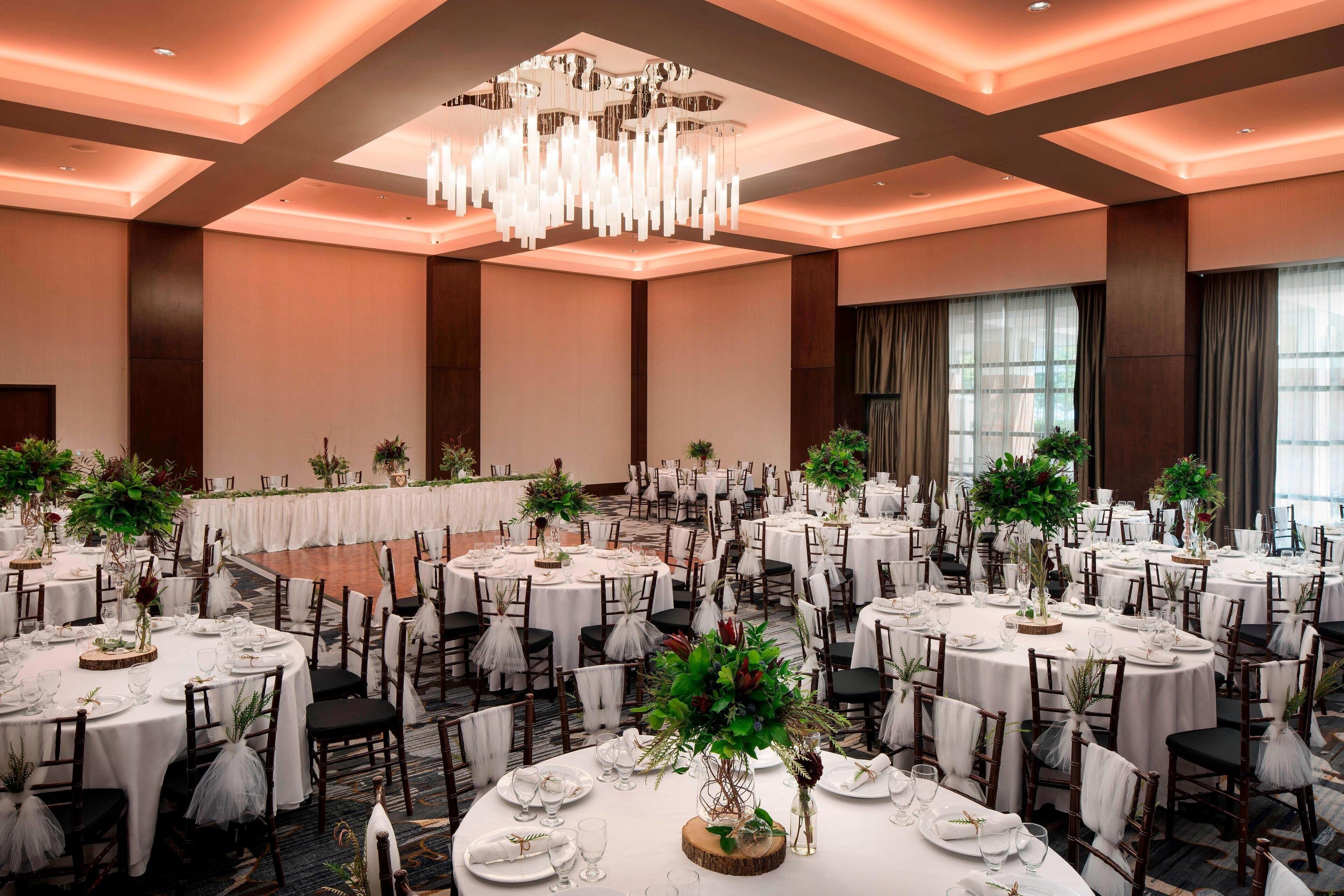 A banquet hall with round tables, white tablecloths, and floral centerpieces.