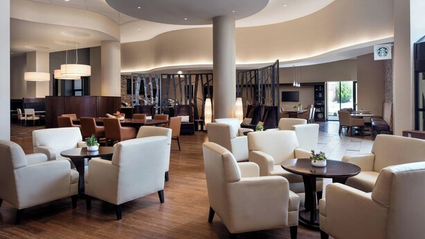 A spacious lobby with modern furniture, a central column, and a Starbucks sign. - Provo Marriott Hotel & Conference Center (Provo)