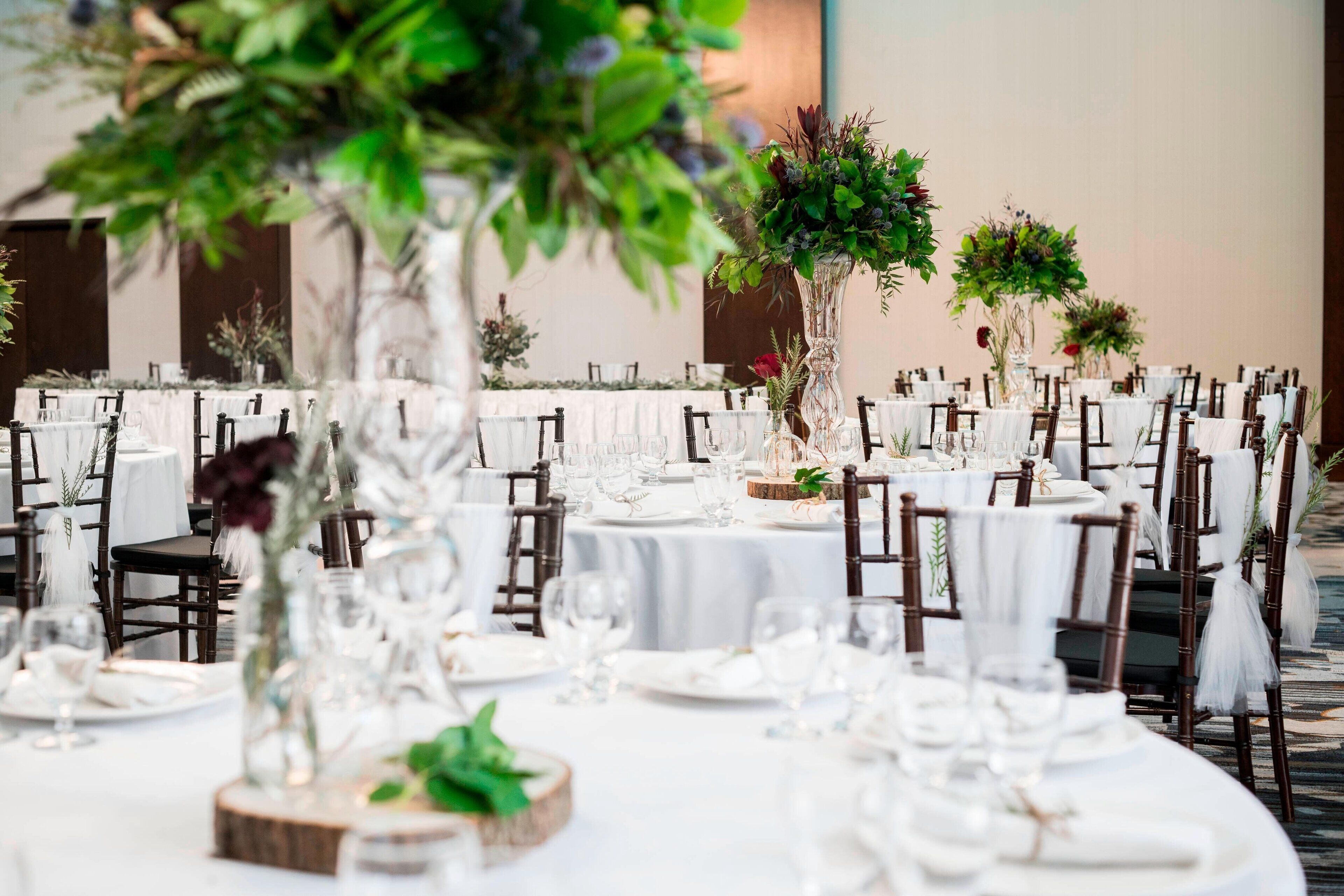 Een feestzaal met ronde tafels, witte tafelkleden en donkerhouten stoelen.