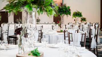 Een feestzaal met ronde tafels, witte tafelkleden en donkerhouten stoelen.