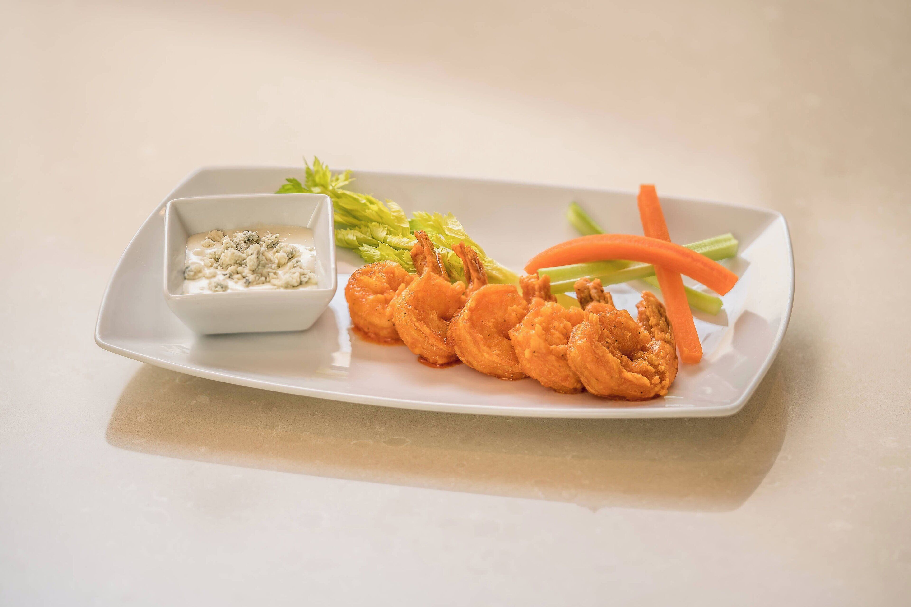 A plate with fried shrimp, celery, carrots, and a small bowl of dipping sauce.