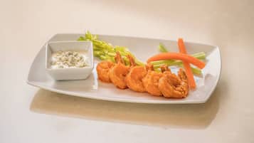A plate with fried shrimp, celery, carrots, and a small bowl of dipping sauce.