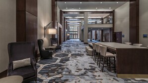 A hotel lobby with a long, patterned carpet, a reception desk, seating areas, and a view of the lobby leading to the entrance. - Provo Marriott Hotel & Conference Center (Provo)