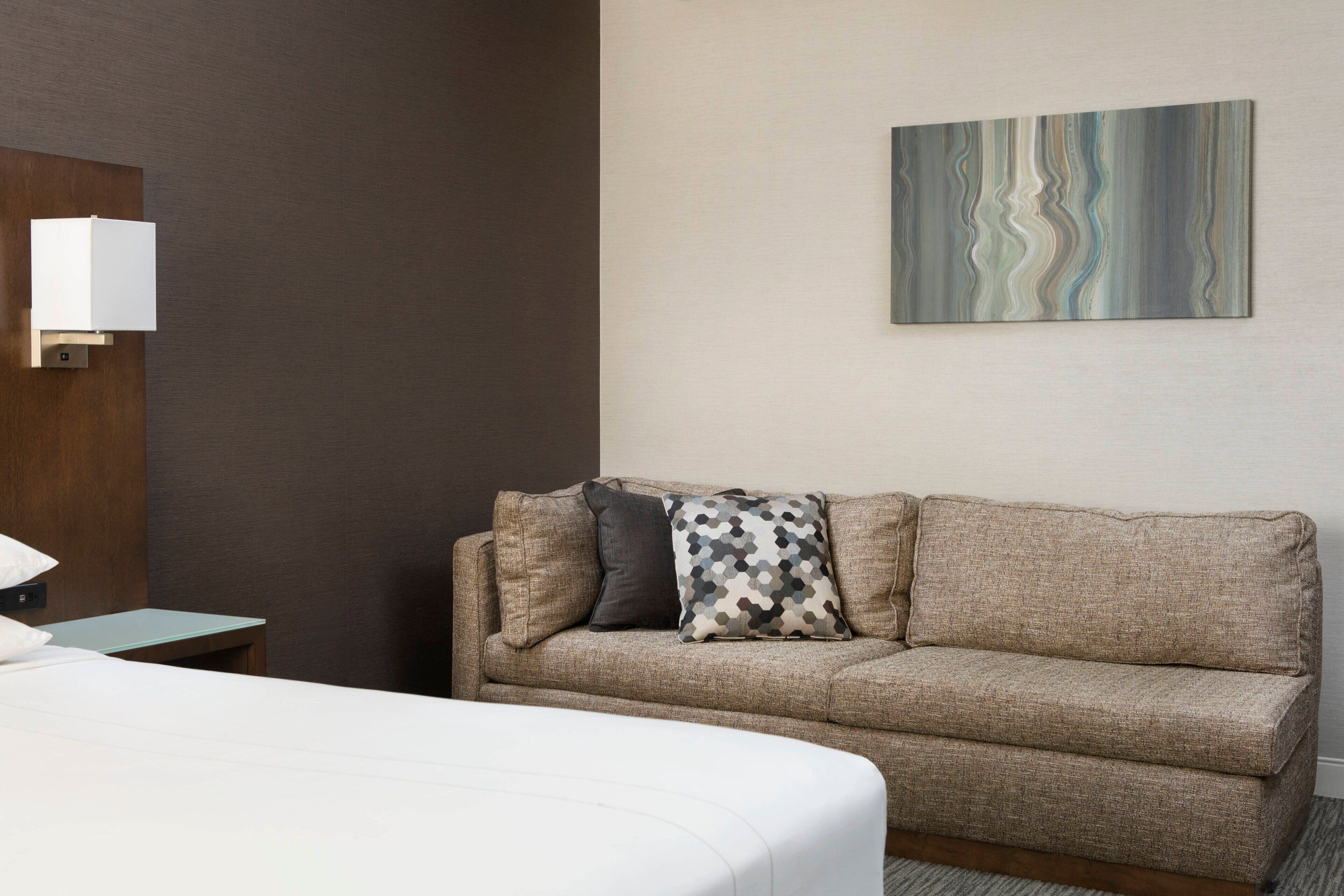 Ein Hotelzimmer mit Bett, einer Couch, einem kleinen Tisch und einem Wandbild.