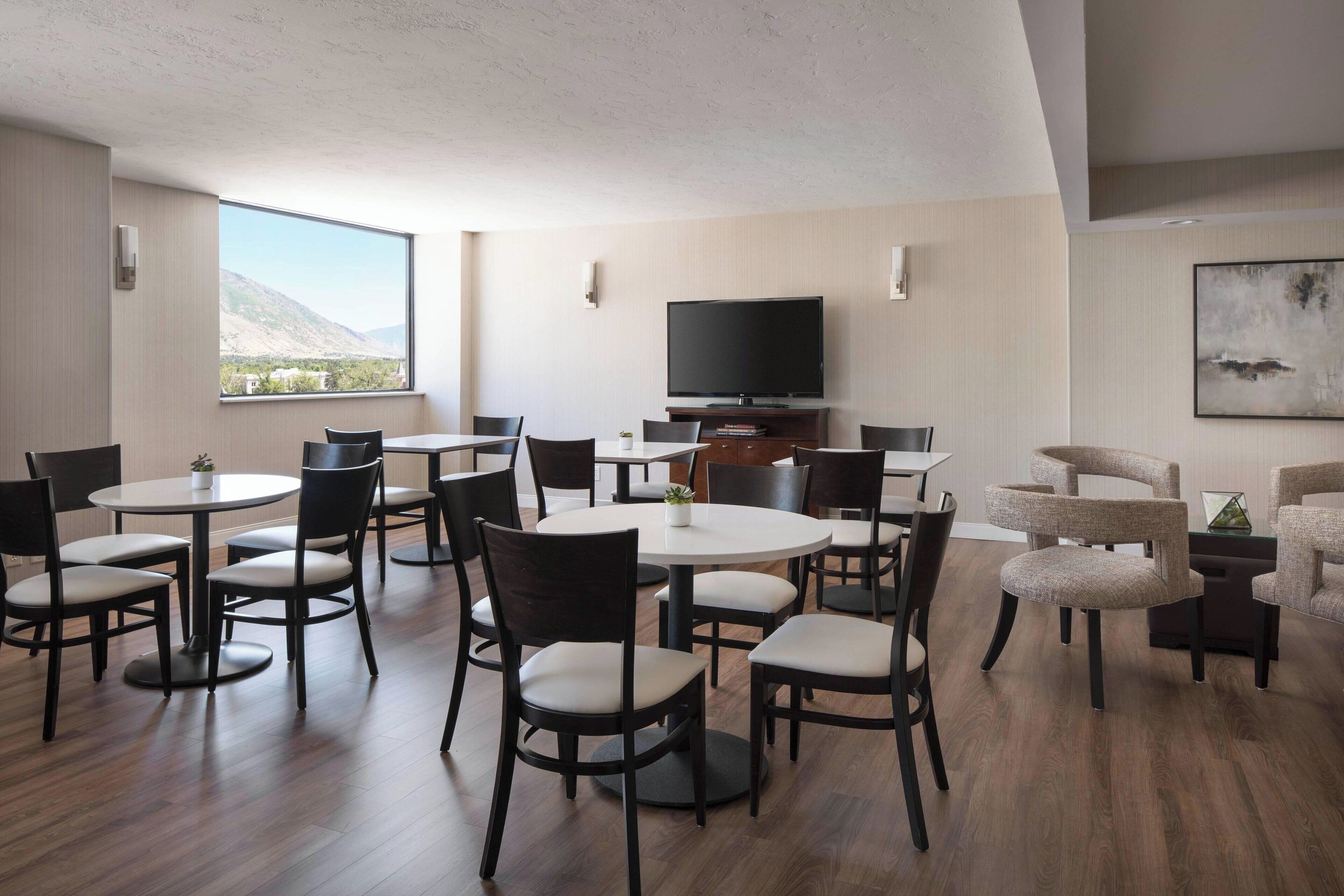 Un'area pranzo moderna con tavoli e sedie rotonde, una televisione a schermo piatto e vista sulle montagne.