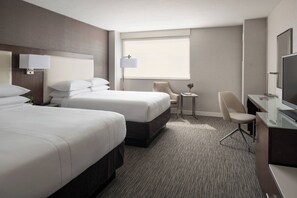 Une chambre d’hôtel avec deux lits, un bureau avec une chaise, une télévision et une petite table avec une lampe.