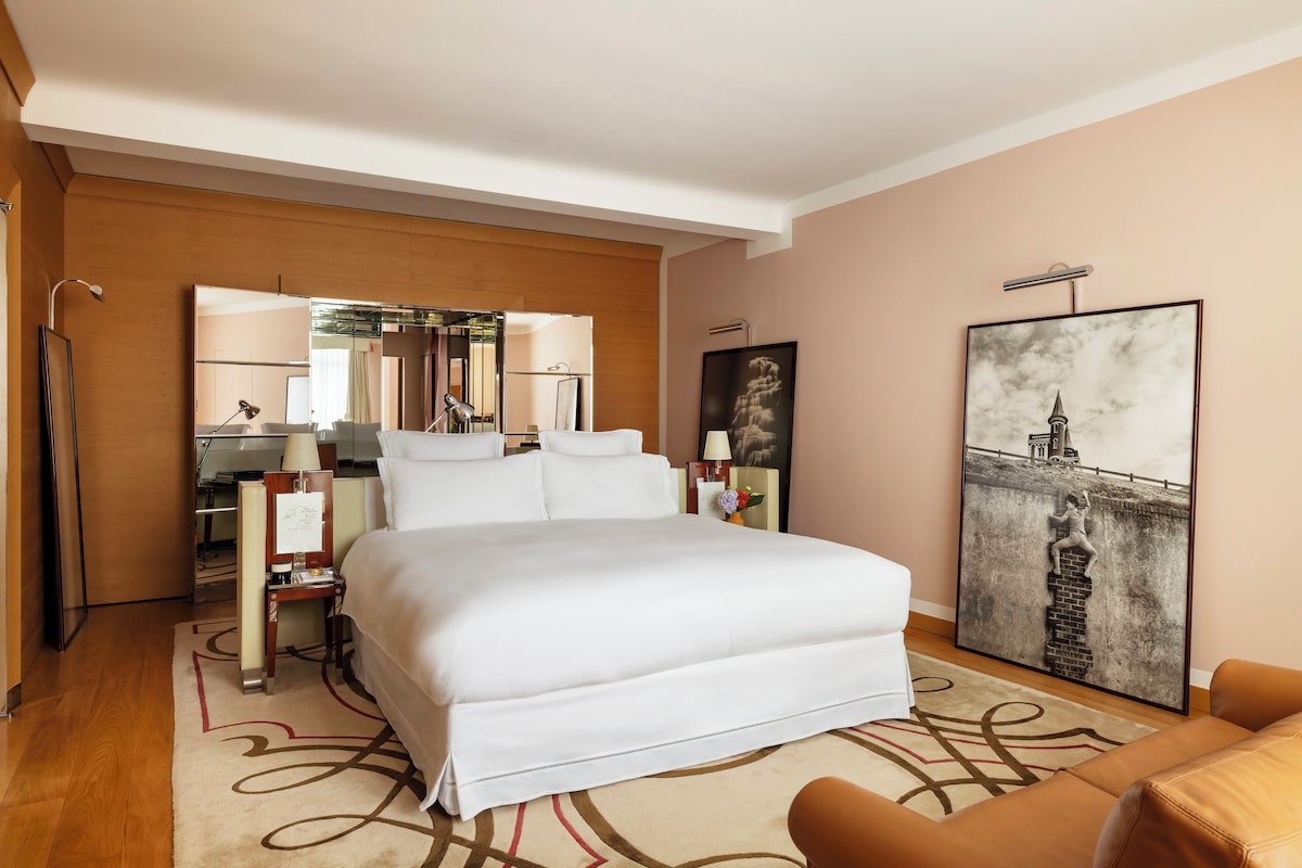 A hotel room with a large bed, a desk with a chair, a mirror, and a framed picture on the wall.