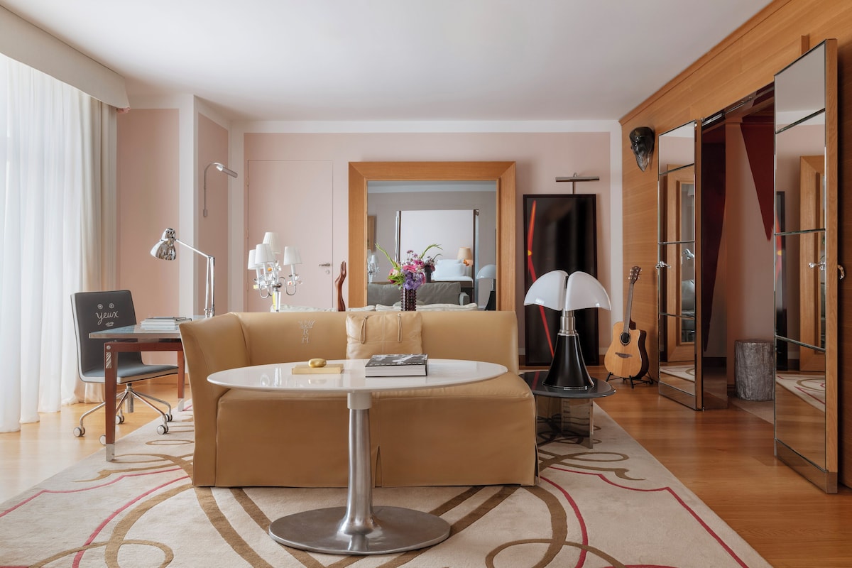 A modern living room with a beige sofa, a round coffee table, and a dining area with a chair and lamp.